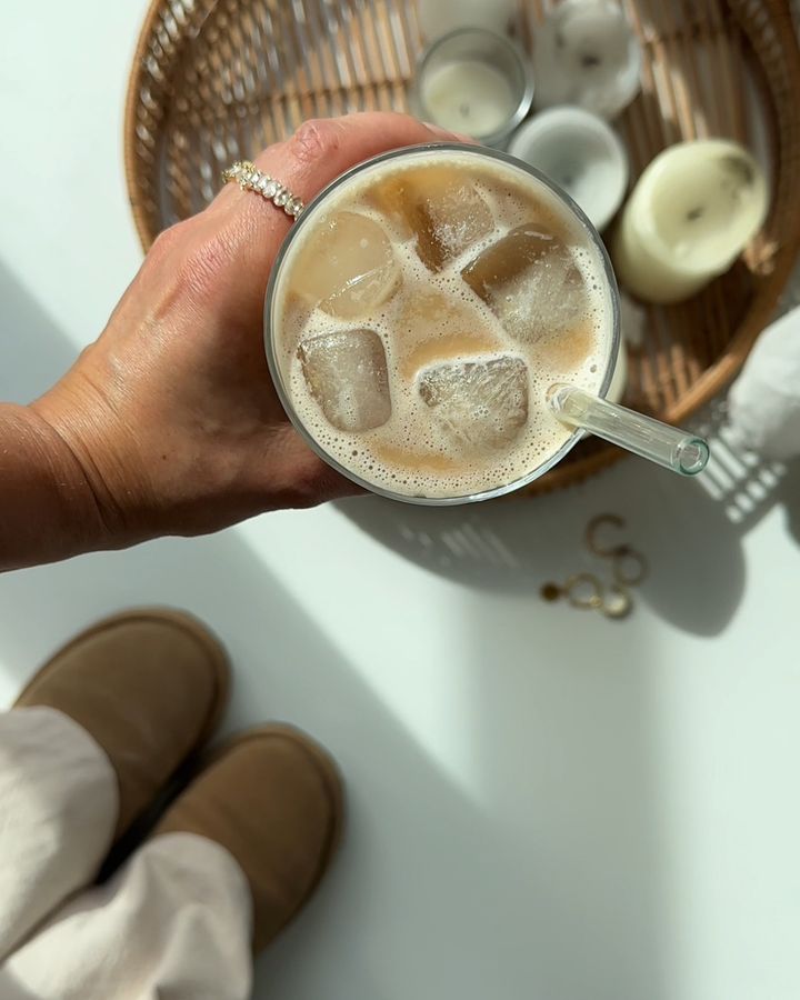 Iced Latte in der Hand, von oben, mit Rattan-Tablett und Kerzen